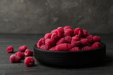 Bowl of delicious fresh ripe raspberries on dark wooden table