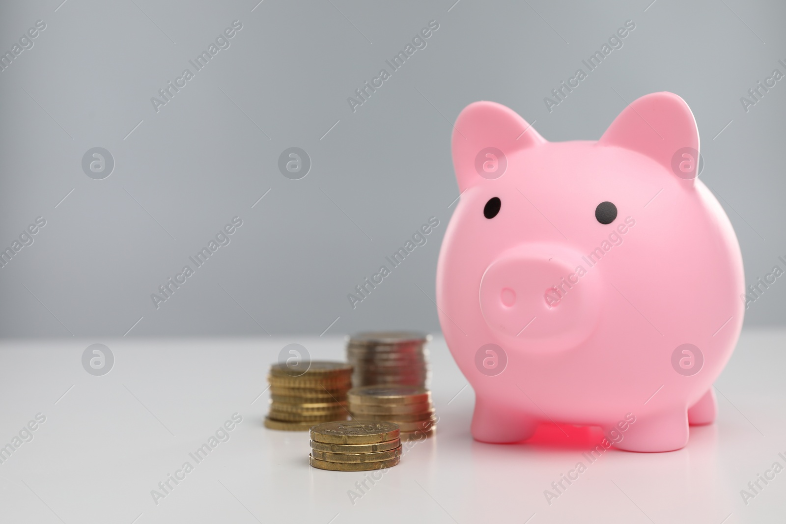 Photo of Pink piggy bank and coins on white table, space for text