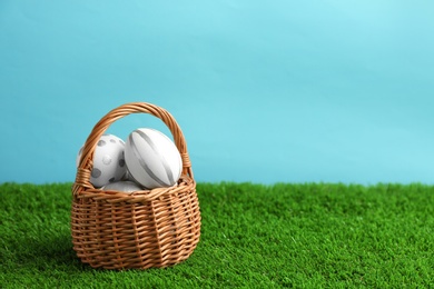 Photo of Wicker basket of painted Easter eggs on green lawn against color background, space for text