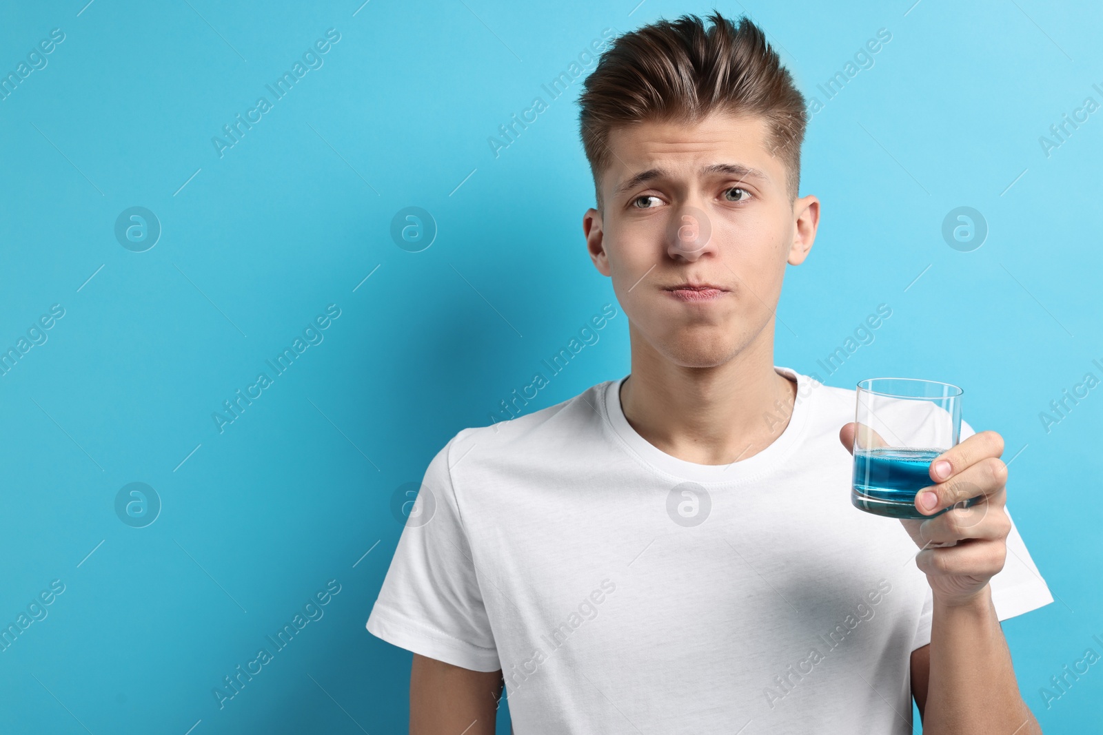 Photo of Young man using mouthwash on light blue background