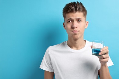 Photo of Young man using mouthwash on light blue background