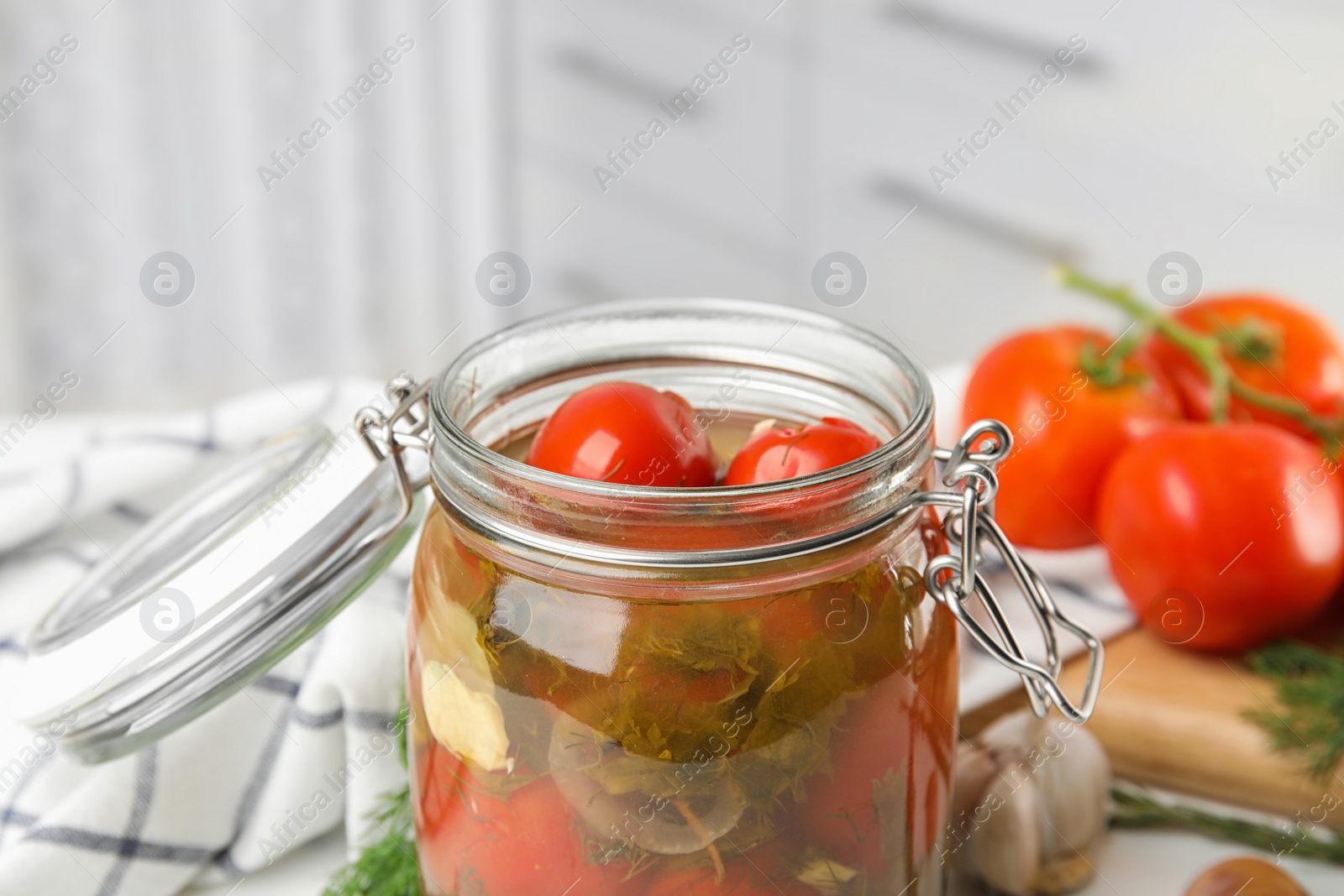 Photo of Pickled tomatoes in glass jar and products on kitchen table, closeup view