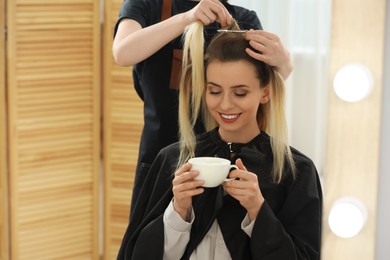 Photo of Hair styling. Professional hairdresser working with woman while she drinking coffee in salon, closeup