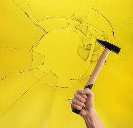Image of Man with hammer breaking up glass against yellow background. closeup 