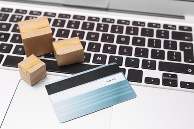 Photo of Internet shopping. Small cardboard boxes and credit card on laptop, closeup