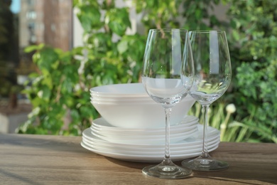 Photo of Clean dishes and glasses on wooden table against blurred background