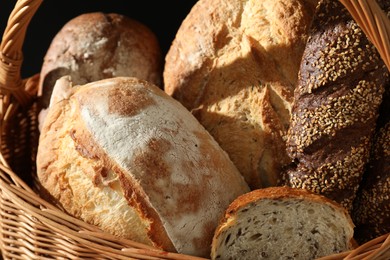 Photo of Wicker basket with different types of fresh bread on dark background, closeup