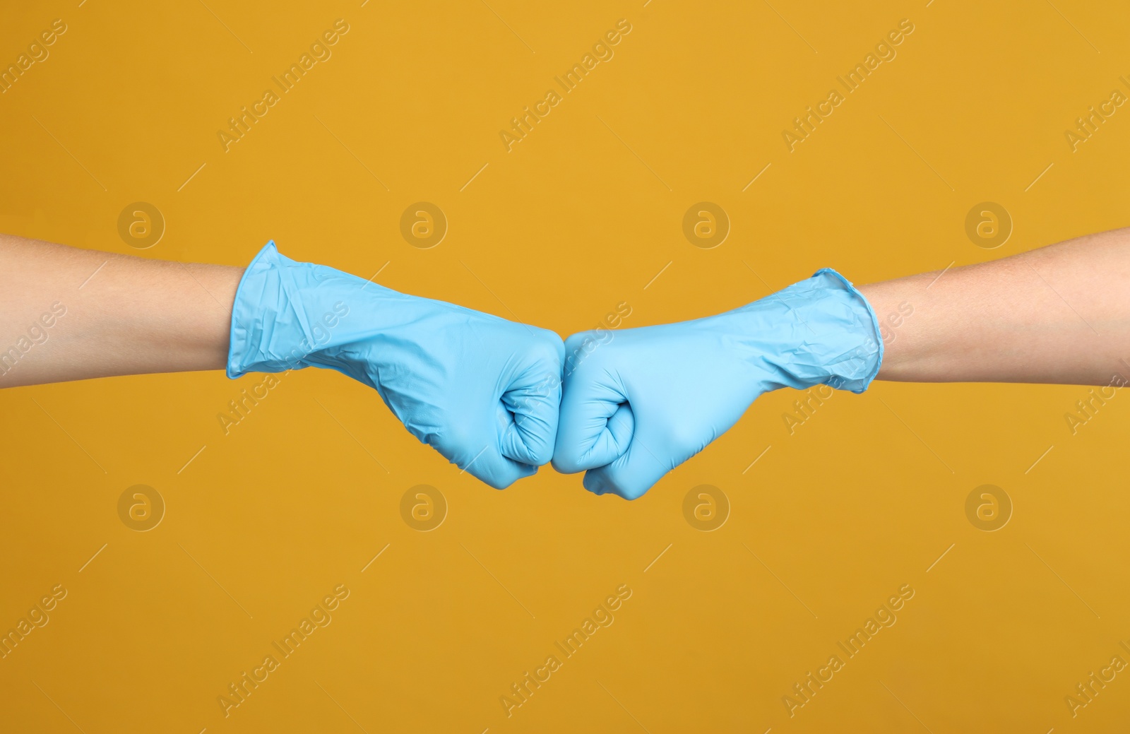 Photo of Doctors in medical gloves making fist bump on yellow background, closeup