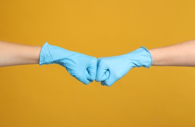 Photo of Doctors in medical gloves making fist bump on yellow background, closeup