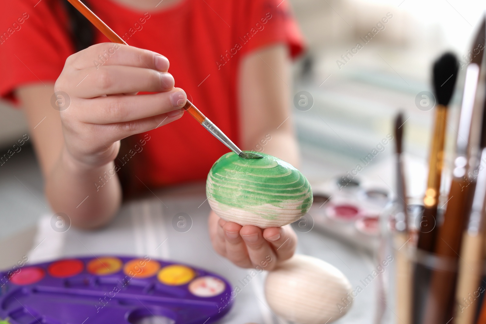 Photo of Little girl painting decorative egg at table indoors, closeup. Creative hobby