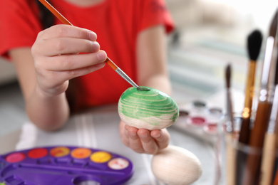Photo of Little girl painting decorative egg at table indoors, closeup. Creative hobby