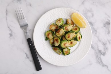 Photo of Delicious roasted Brussels sprouts, slice of lemon and fork on white marble table, top view