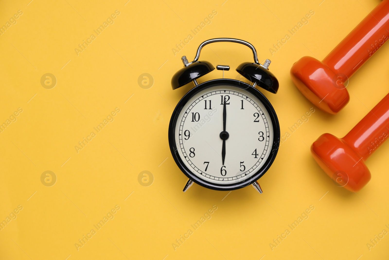 Photo of Alarm clock and dumbbells on yellow background, flat lay with space for text. Morning exercise