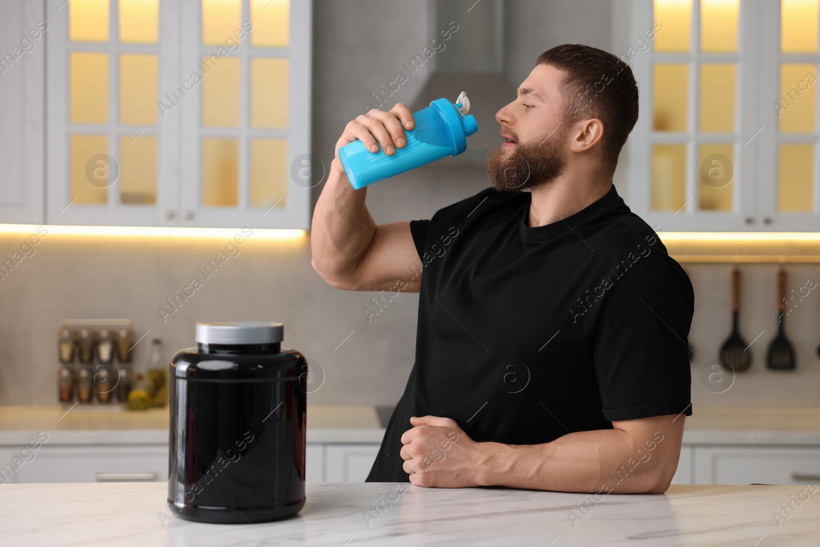 Photo of Young man with shaker of protein and powder at white marble table in kitchen