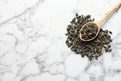 Photo of Tie Guan Yin oolong tea leaves and spoon on marble background, top view. Space for text