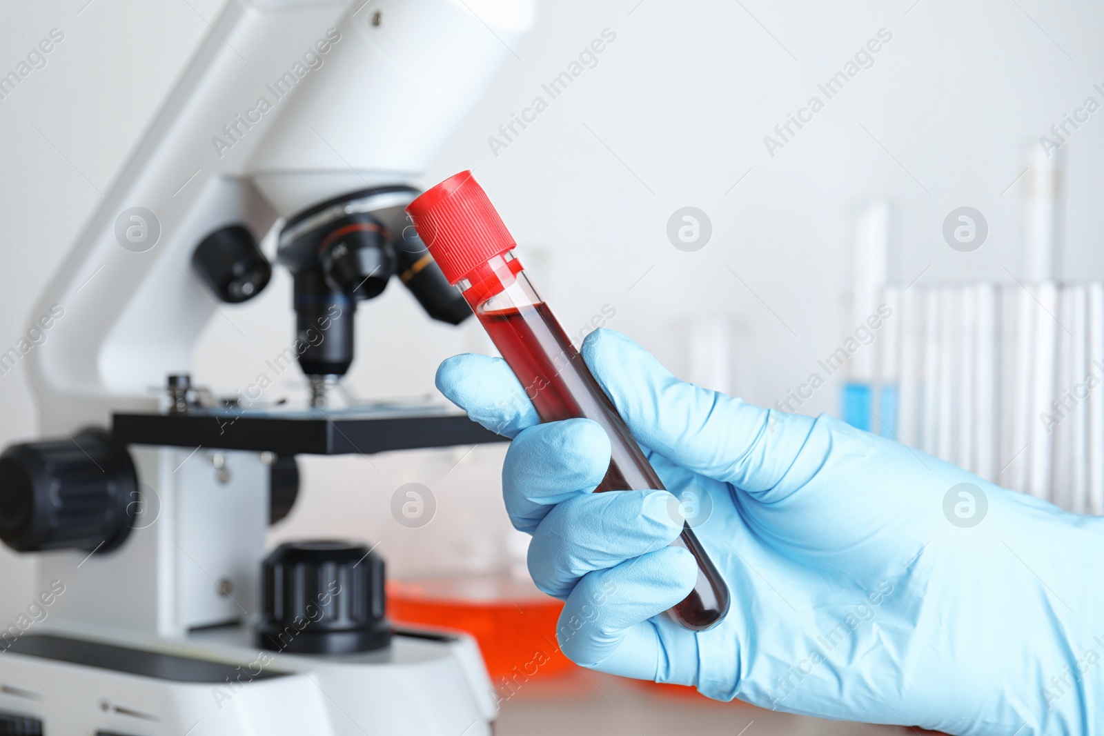 Image of Scientist holding test tube with blood sample near microscope, closeup. Laboratory analysis