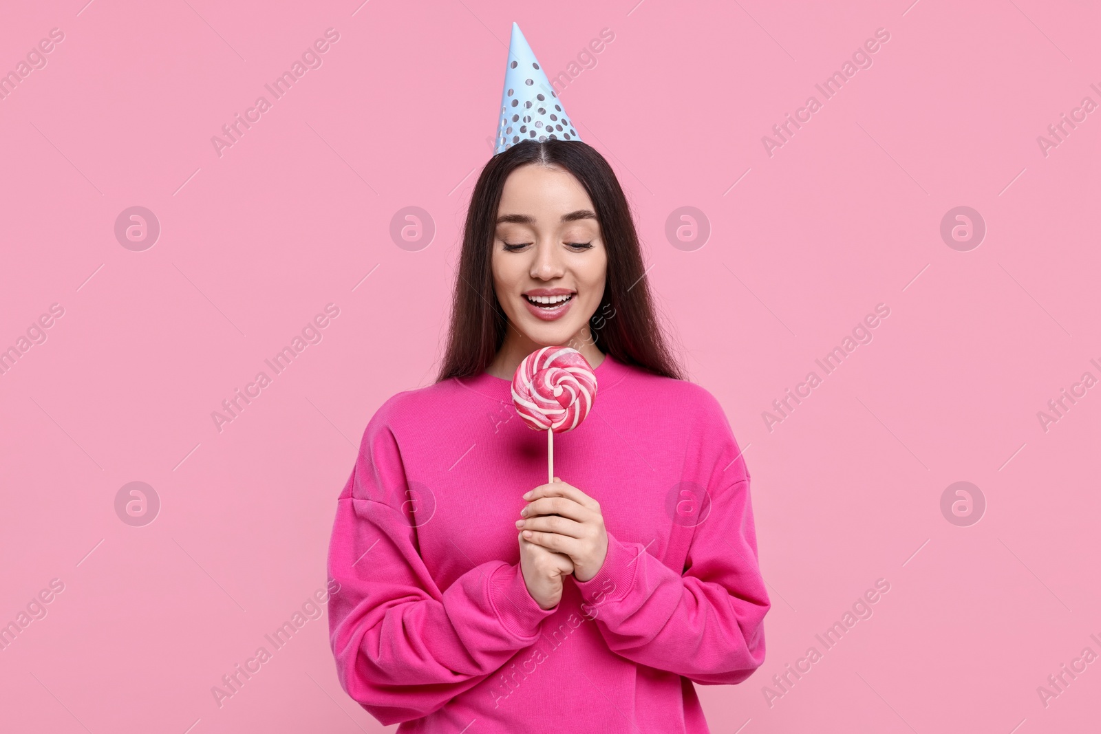 Photo of Woman in party hat holding lollipop on pink background