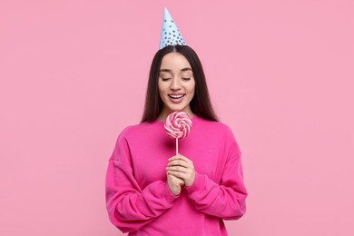 Photo of Woman in party hat holding lollipop on pink background