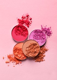 Different crushed eye shadows on pink background, flat lay