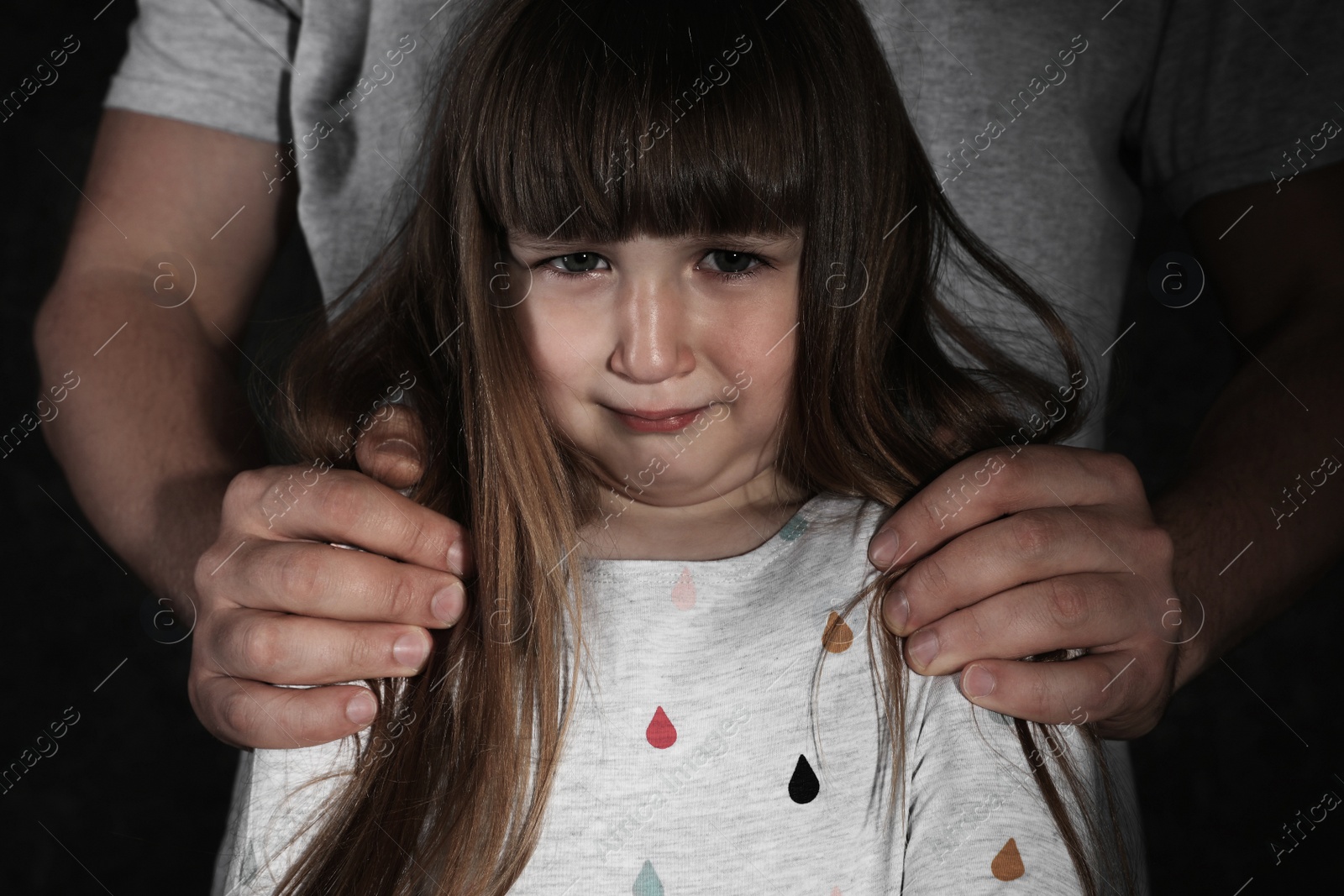 Photo of Crying little girl and adult man on dark background, closeup. Child in danger