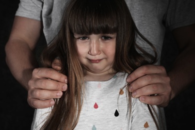 Photo of Crying little girl and adult man on dark background, closeup. Child in danger