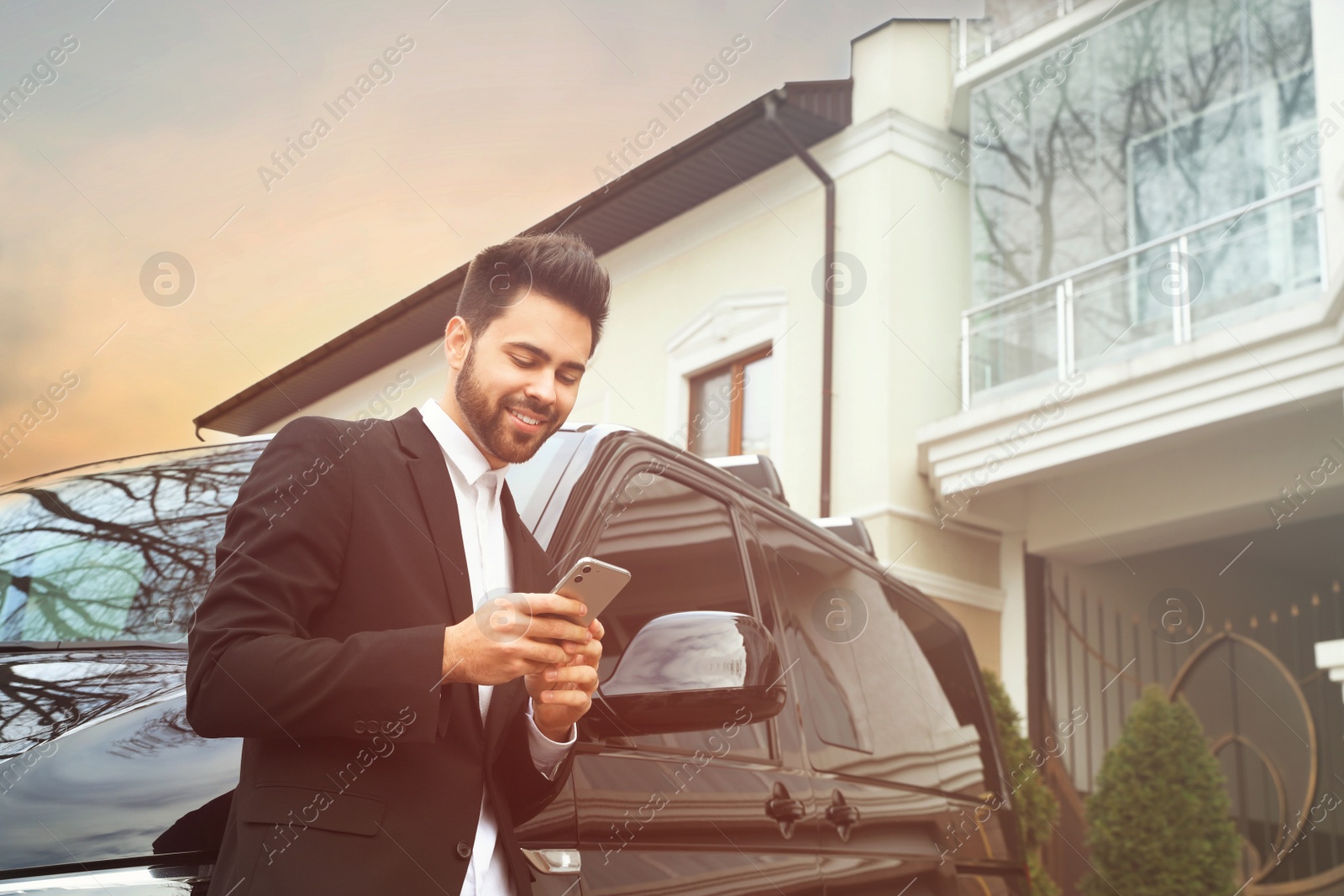 Image of Handsome young man with smartphone near modern car outdoors