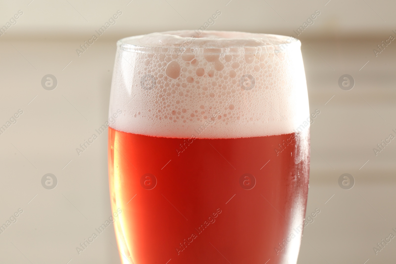 Photo of Glass of red tasty beer with foam, closeup