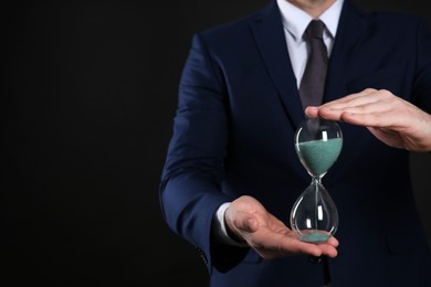 Photo of Closeup view of businessman holding hourglass on black background, space for text. Time management