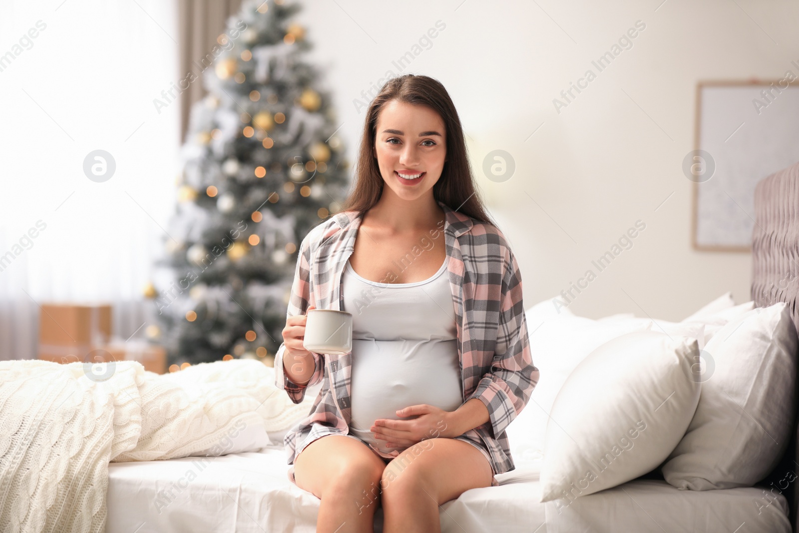 Photo of Happy pregnant woman on bed in room decorated for Christmas. Expecting baby