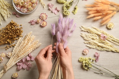 Florist making bouquet of dried flowers at white wooden table, top view