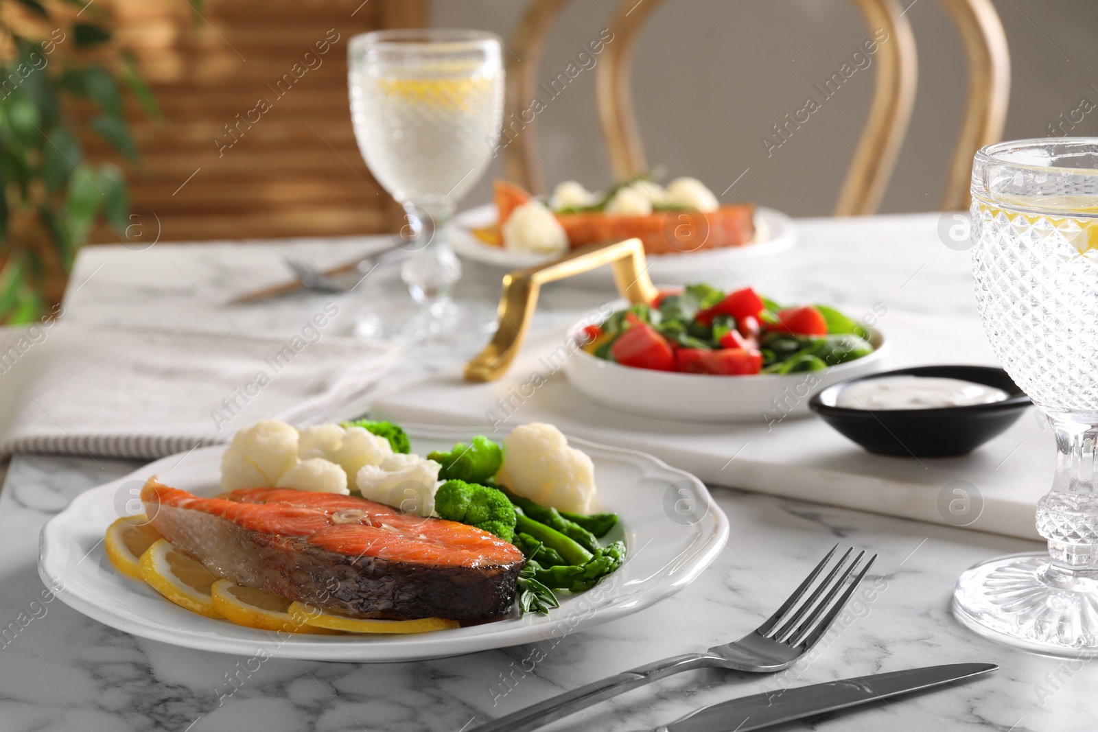 Photo of Healthy meal. Tasty grilled salmon with vegetables and lemon served on white marble table