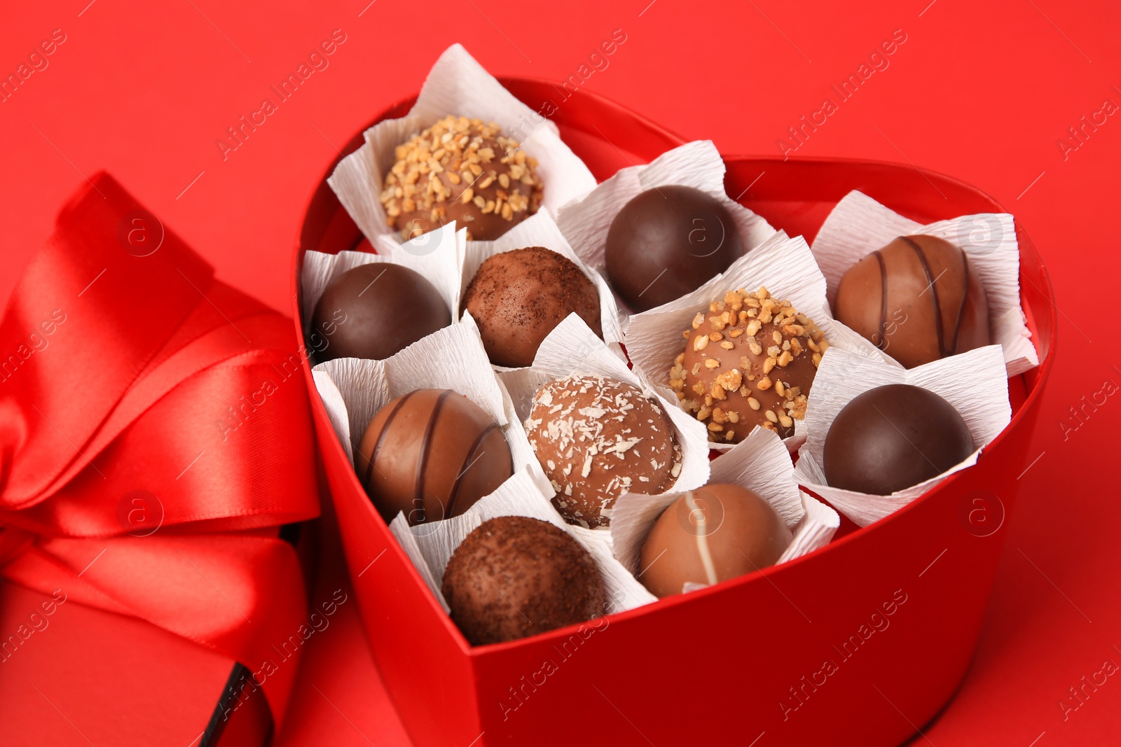 Photo of Heart shaped box with delicious chocolate candies on red table, closeup