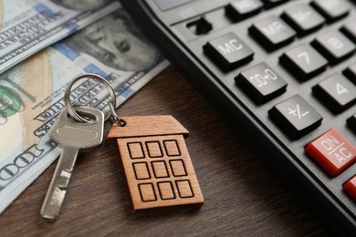 Photo of Mortgage concept. Key with house shaped trinket, calculator and money on wooden table, closeup