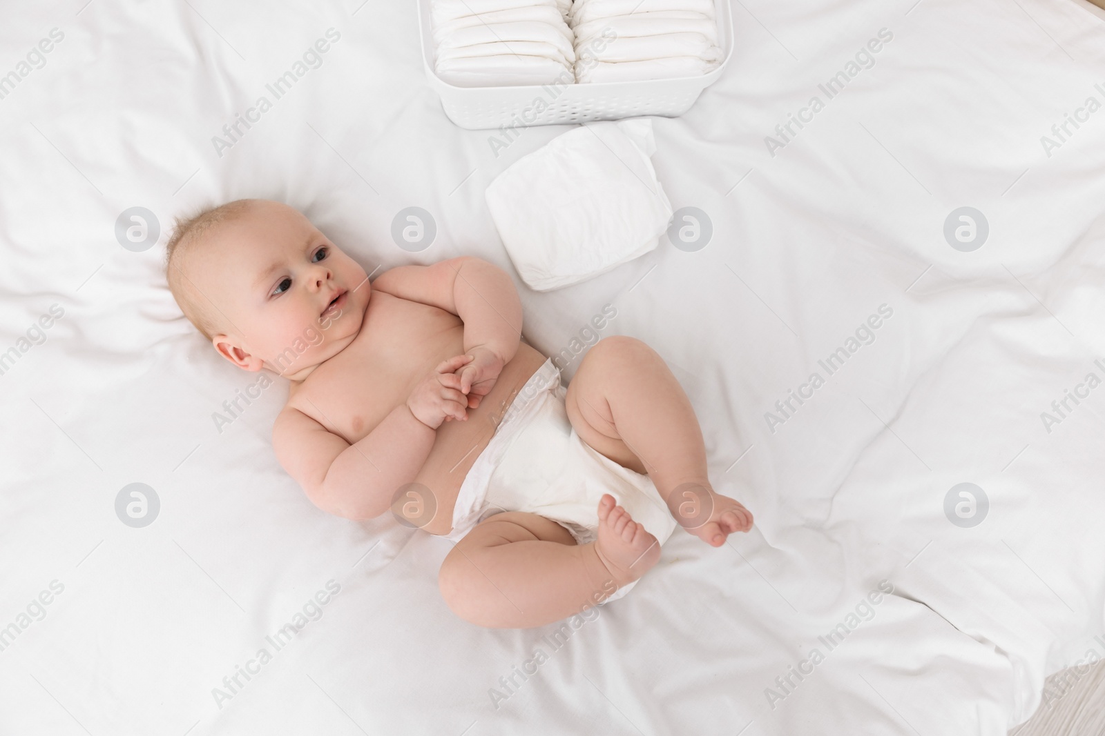 Photo of Cute baby and diapers on white bed, top view