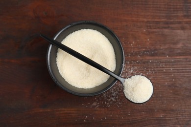 Photo of Gelatin powder in bowl and spoon on wooden table, top view