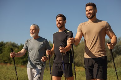 Happy men practicing Nordic walking with poles outdoors on sunny day