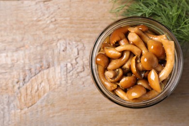 Photo of Delicious marinated mushrooms in glass jar and dill on wooden table, flat lay. Space for text