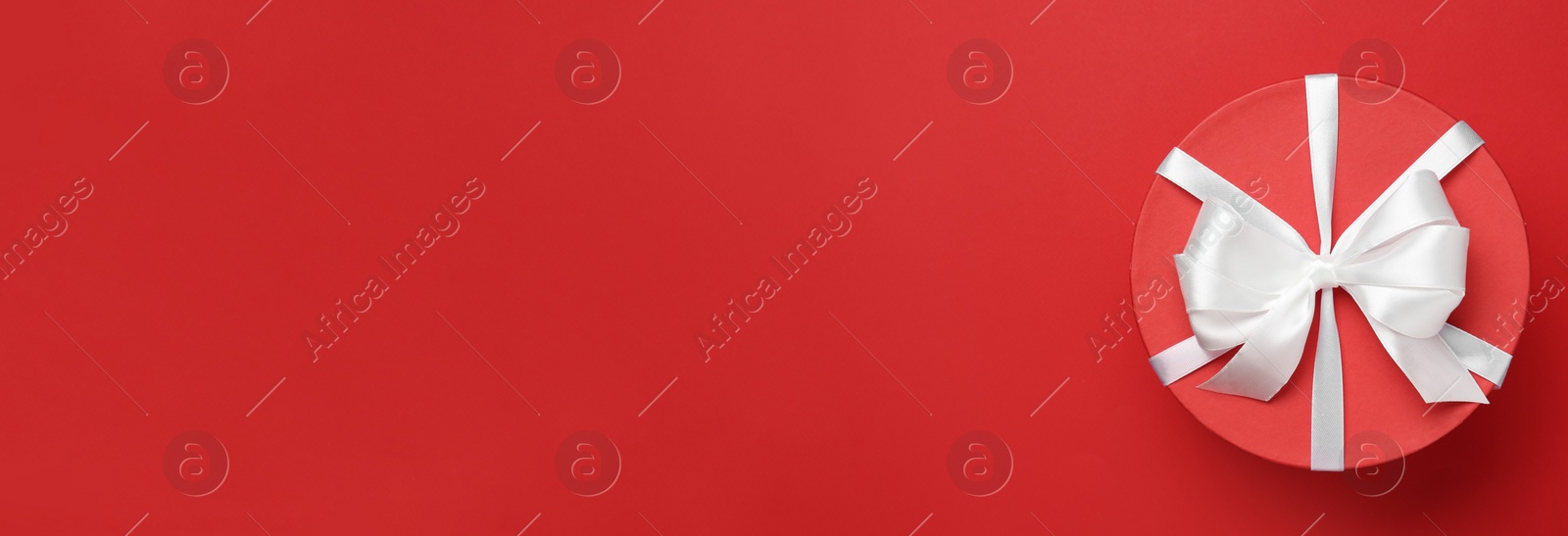 Photo of Beautiful gift box with white bow on red background, top view. Space for text