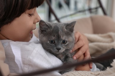 Photo of Cute little boy with kitten in chair at home, closeup. Childhood pet