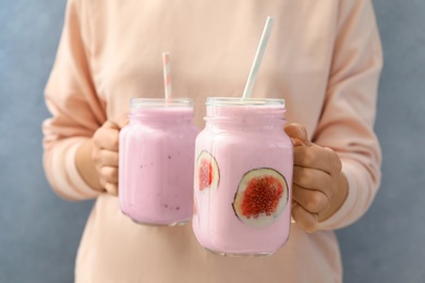 Photo of Woman holding fig smoothie on light blue background, closeup