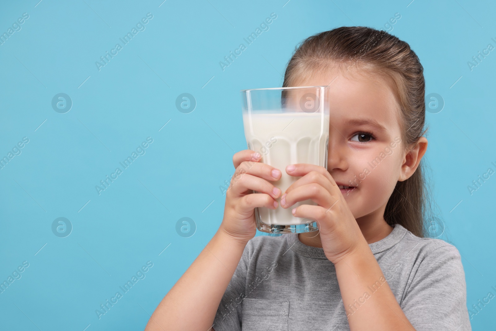 Photo of Cute girl with glass of fresh milk on light blue background, space for text