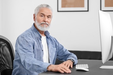 Photo of Handsome senior man working on computer at table in office. Space for text