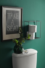 Decor elements, paper rolls and toilet bowl near green wall. Bathroom interior