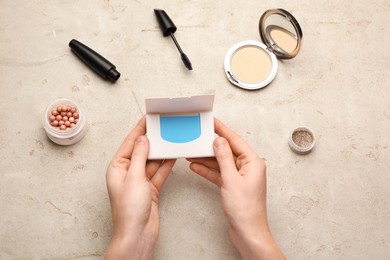Photo of Woman with package of oil blotting tissues and decorative cosmetics at light grey table, top view. Mattifying wipes
