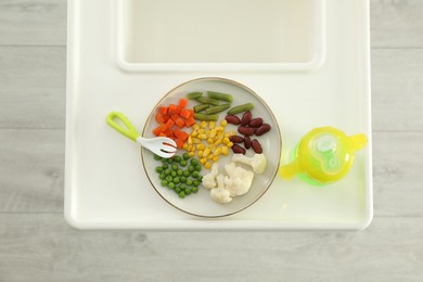 Photo of Baby high chair with healthy food and water, top view