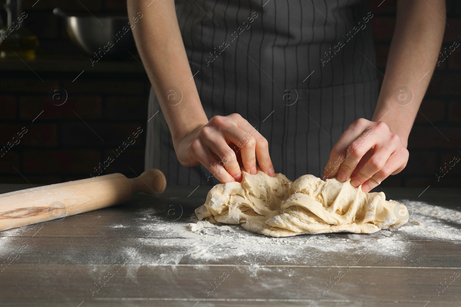 Photo of Making bread. Woman kneading dough at wooden table in kitchen, closeup