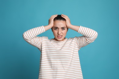 Photo of Young woman suffering from headache on light blue background