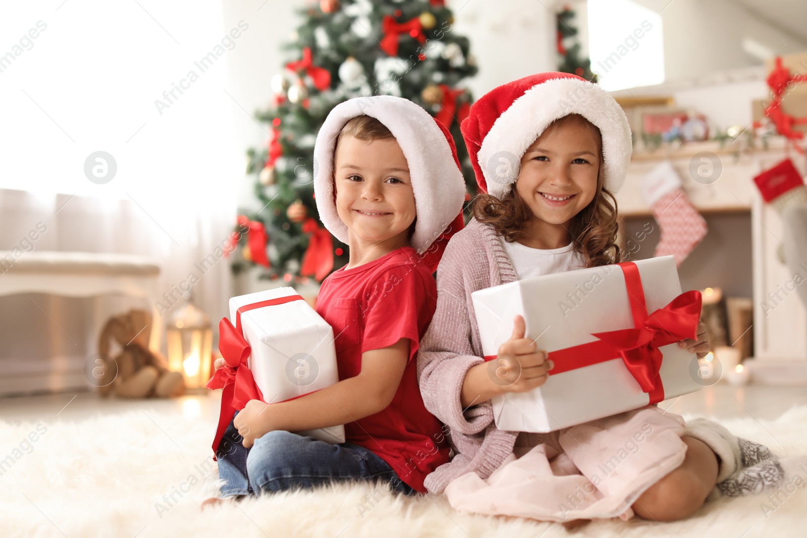 Photo of Cute little children in Santa hats with Christmas gift boxes at home