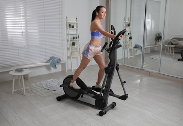 Happy young woman training on elliptical machine at home