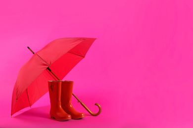 Photo of Beautiful red umbrella and rubber boots on pink background